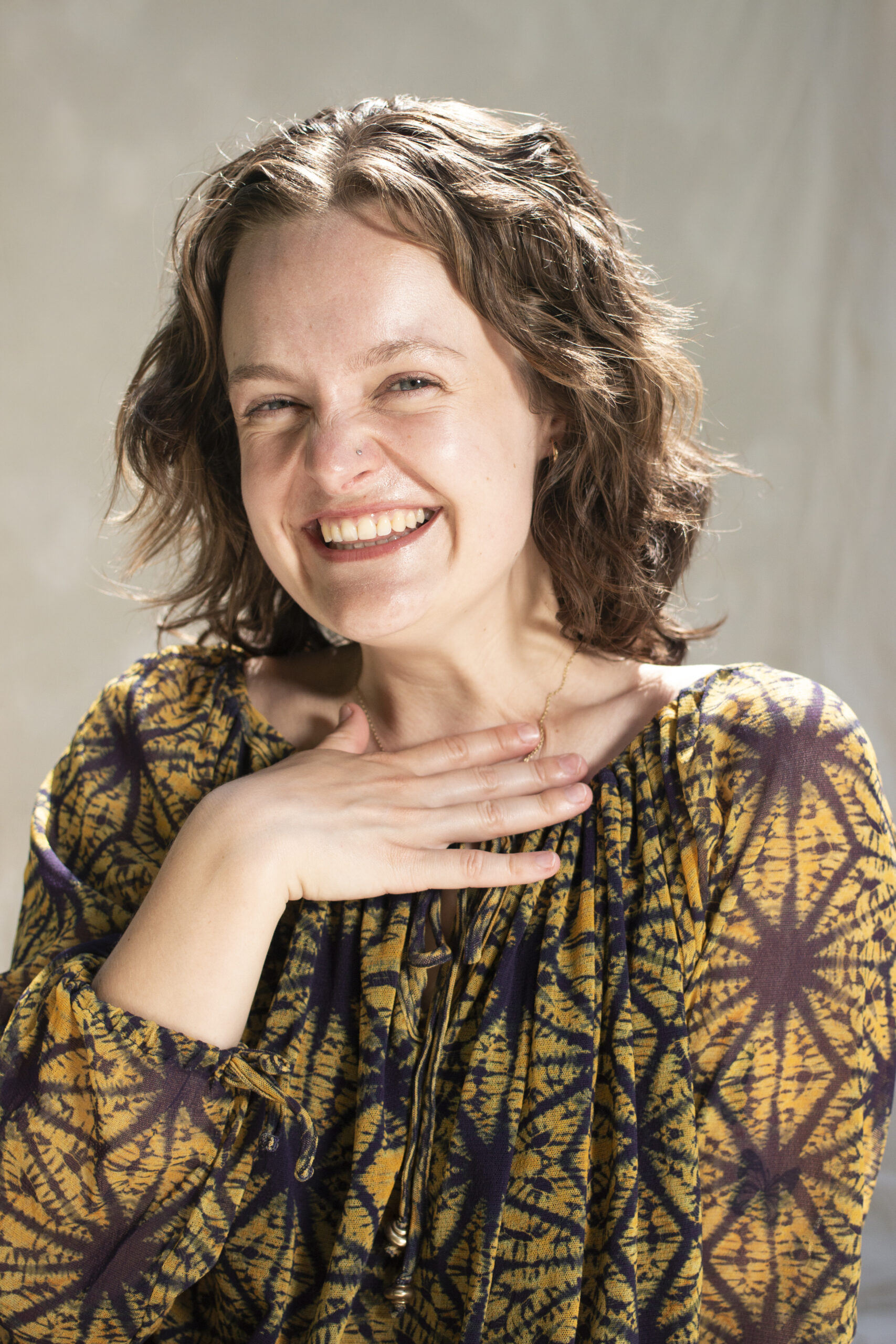 Photo of Frances smiling widely. She is wearing a yellow and navy top and is in the sun.